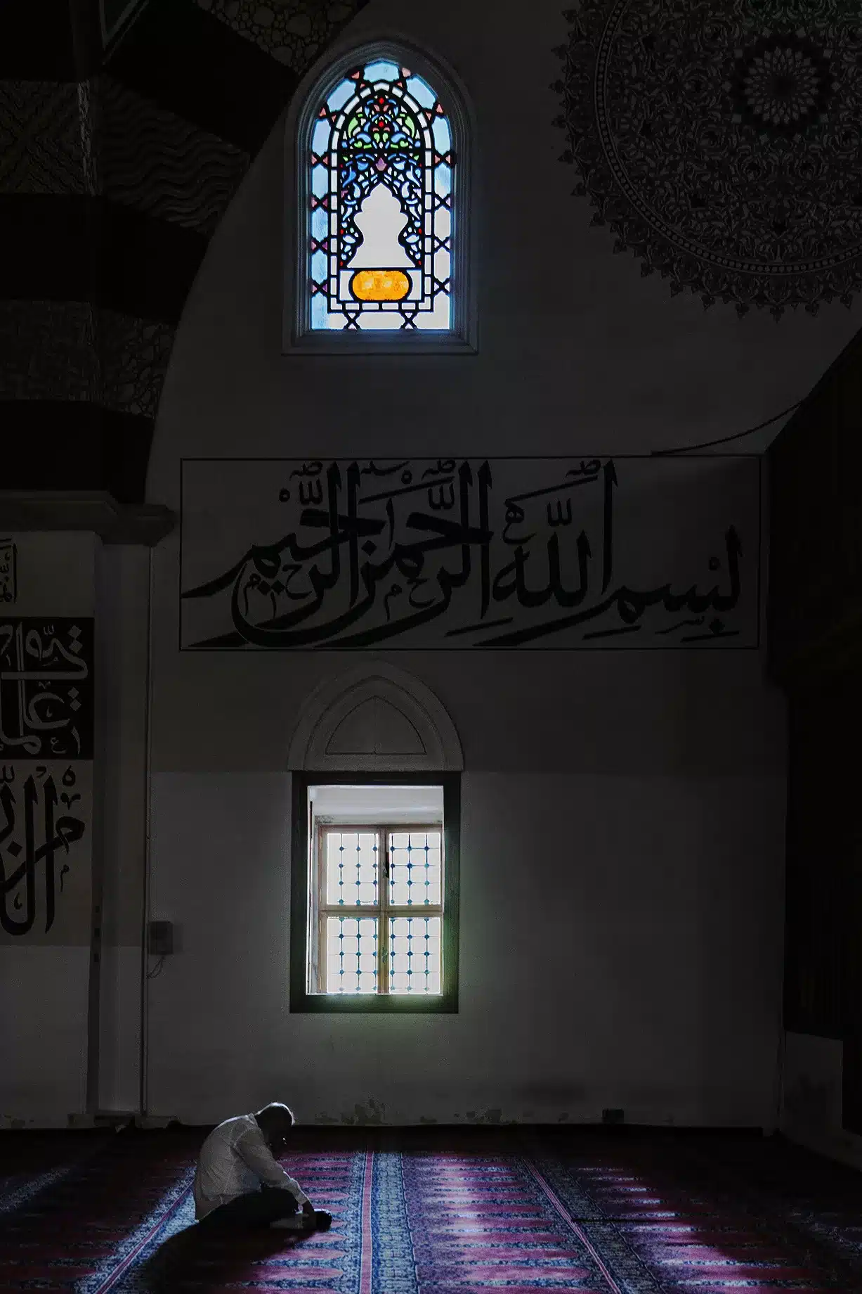 la prière Homme priant dans une mosquée en Albanie, éclairé par la lumière entrant par les fenêtres.